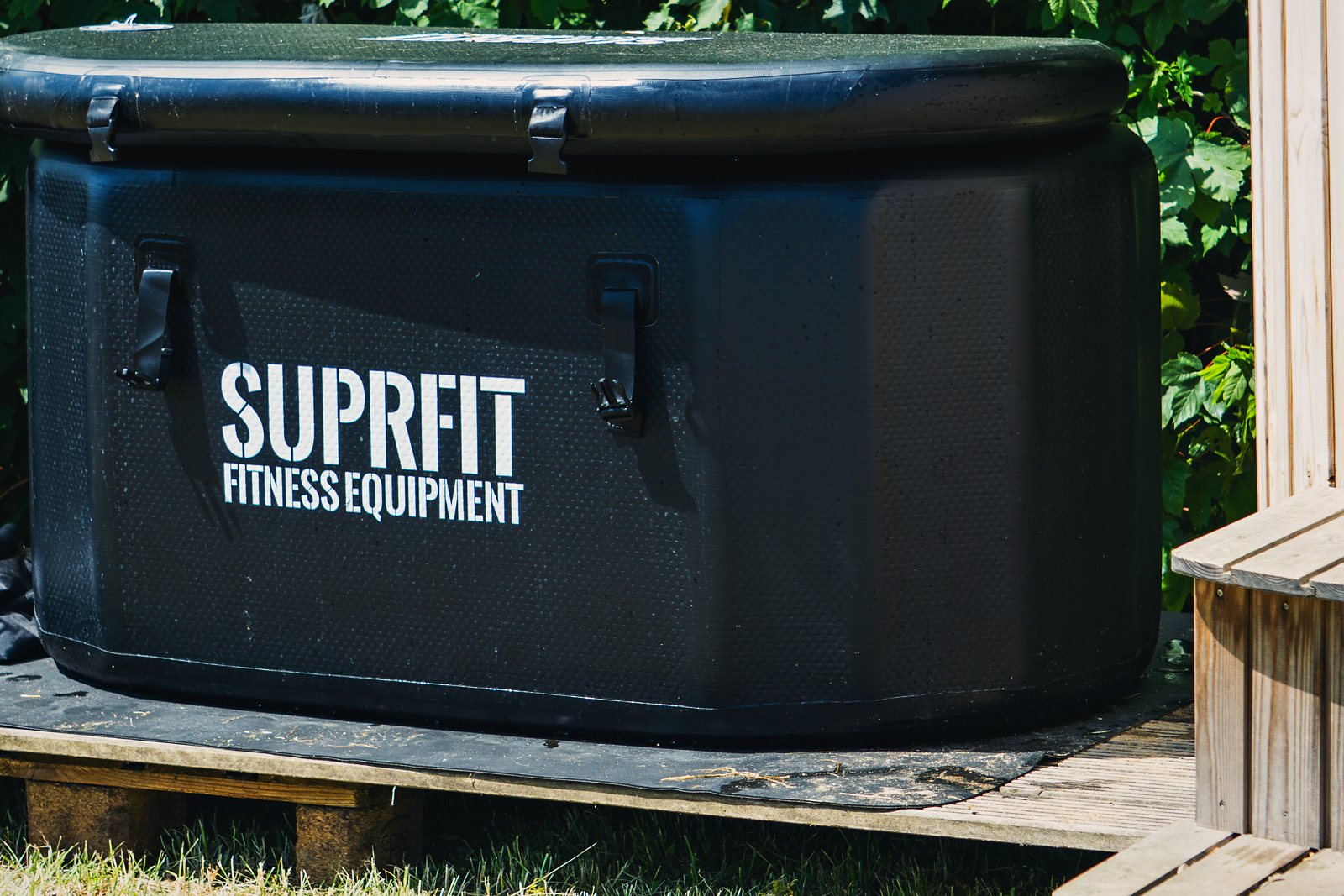Eine schwarze, eckige Eiswanne mit weißem SUPRFIT-Logo steht vor einer grünen Hecke